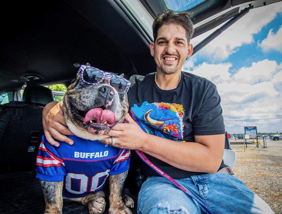 David Singh and Famous, wearing a Buffalo Bills jersey and star sunglasses, sit in an open tailgate.
